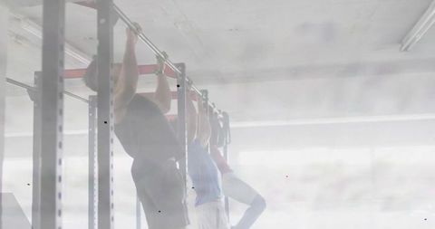 Backlit athletes performing pull-ups on rig in mist-filled gym, strength training trio