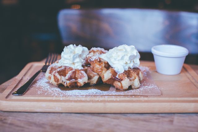 Belgian waffles garnished with whipped cream and sprinkled with powdered sugar served on a wooden tray, perfect for breakfast or dessert promotions on social media, food blogs, menus, or recipe books.