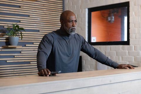 Mature man leaning at modern reception desk with smartphone, minimalist lobby scene