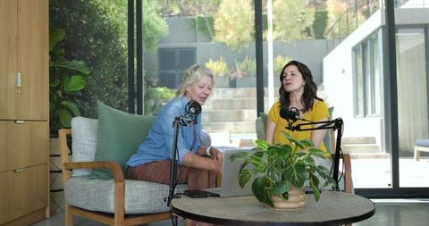 Diverse women recording podcast in sunlit modern living room with laptop and microphones