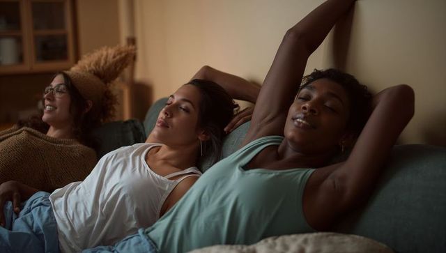 Three friends relaxing on sofa in cozy living room evening, casual lounge friendship