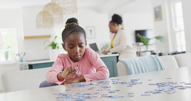 Happy african american granddaughter doing jigsaw puzzle, with grandmother in background, copy space. Relaxation, learning, family and domestic life.
