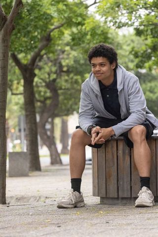 Contemplative african american man sitting on wooden bench under urban tree canopy