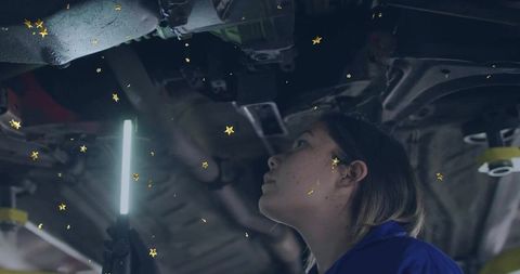 Female auto technician examining car undercarriage with led light