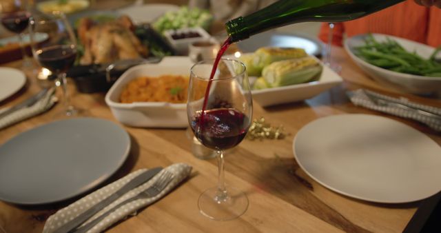 Red wine is poured into a glass at a festive dinner table. A sumptuous feast suggests a celebration or holiday meal at home.