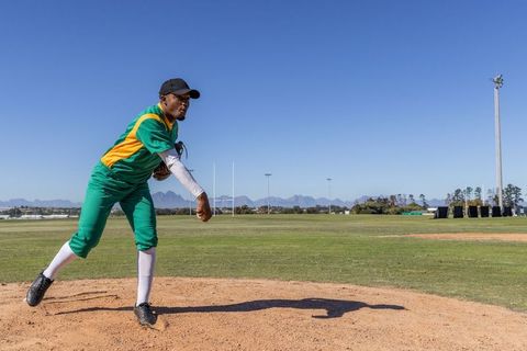 African American Baseball Pitcher Delivering Pitch on Dirt Mound with Mountain Background