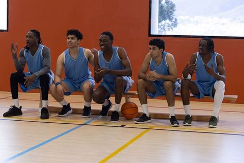 Basketball team in uniforms relaxing enthusiastically on bench