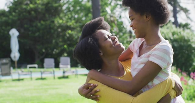 African American mother and daughter enjoying a moment of love and affection in a park. The mother is holding her daughter as they smile and look at each other, showcasing a beautiful family bond. Great for themes around family, relationships, parenting, and childhood, this positive and heartwarming scene can be used in family-oriented advertisements, social media posts, and articles about parenting tips.