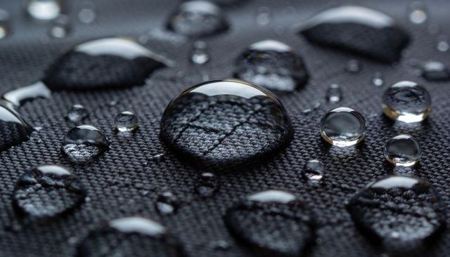 Macro beading water droplets revealing woven black textile texture and crisp reflections