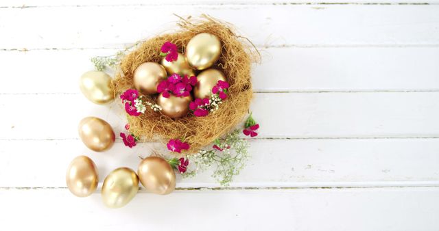Golden eggs are nestled in a nest with vibrant pink flowers on a white wooden background, with copy space. Symbolizing wealth and prosperity, the image is often associated with Easter or financial concepts.