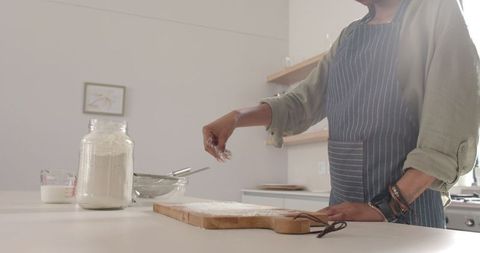 Woman in Striped Apron Sprinkling Flour in Modern Kitchen