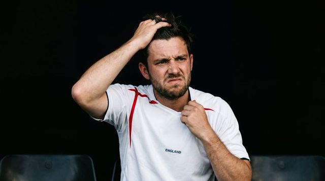 Frustrated england fan tugging collar and running fingers through hair on bench, moody