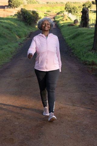 African american senior woman walking joyfully on rural trail under sunlight