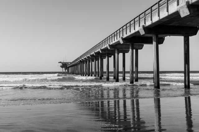This image showcases a pier extending into the sea with clear reflections in the water. The black and white tones emphasize the serene and tranquil atmosphere. Useful for projects related to travel, seaside retreats, architecture, and hobbies such as photography. Ideal for backgrounds, inspirational posters, and website headers.