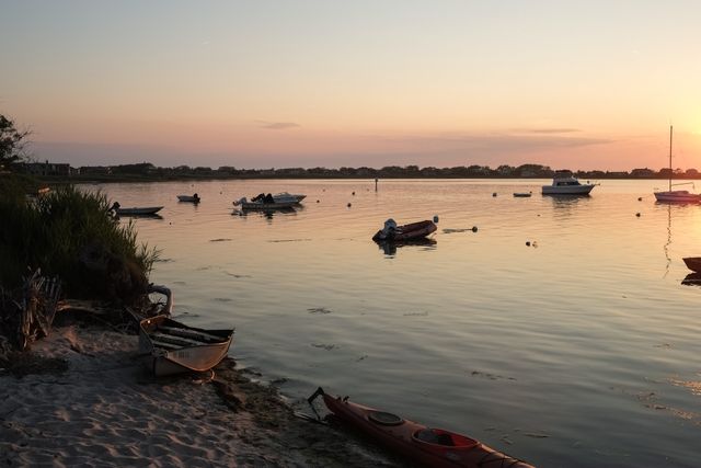 Lakeside view during sunset with boats and canoes resting by the shore, creating a serene and tranquil scene. Ideal for use in travel blogs, nature websites, relaxation-themed publications, and for promoting peaceful getaways.