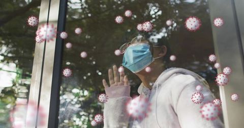Child pressing hand to window wearing face mask and glasses gazing out at virus icons