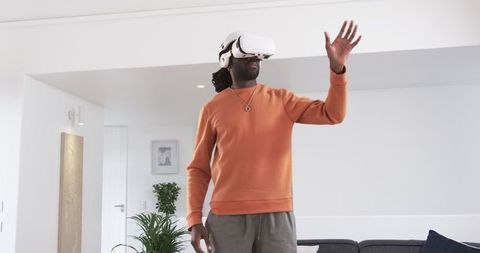 African american man using vr headset, reaching for virtual controls in modern living room