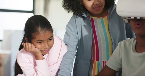 Teens exploring virtual reality together, collaborating around vr headset in classroom