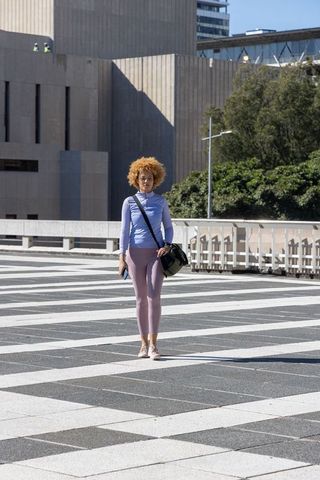 Young african american woman standing on geometric urban plaza holding phone and bag