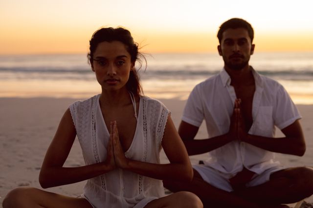 Portrait of couple performing yoga together on the beach