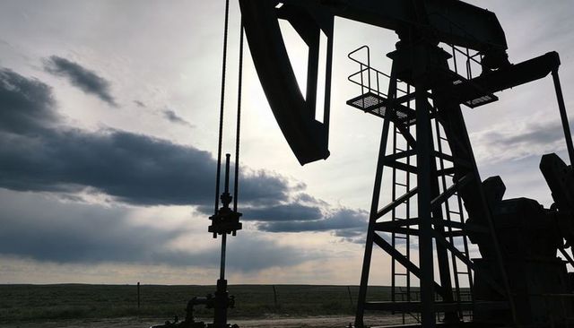 Oil pumpjack silhouetting on prairie horizon at sunset with dramatic backlit clouds