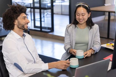 Diverse coworkers enjoying coffee and birthday celebration at office desk