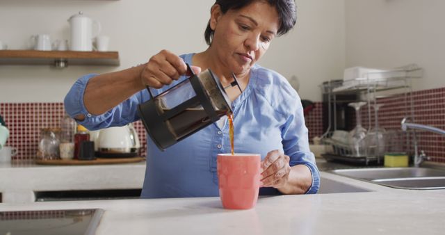 Asian senior woman pouring coffee in her cup in the kitchen at home. retirement lifestyle and living concept