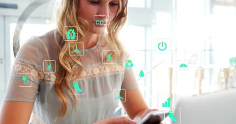 Woman scrolling smartphone with green sustainability icons overlay in bright modern workspace