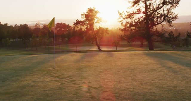 Capturing the serene atmosphere of a golf course at sunrise with a green flag on the field. Perfect for brochures, websites, or advertisements related to golf, outdoor activities, relaxation, or nature. Ideal for presenting the beauty of early morning tee time or promoting peaceful outdoor settings.