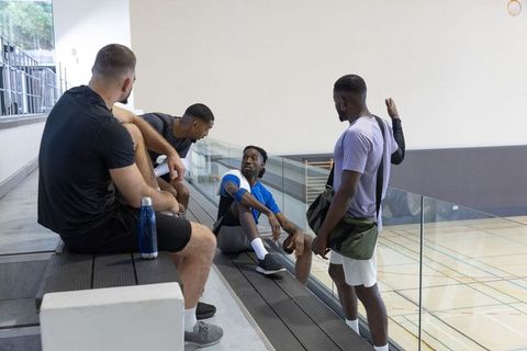Mens team chatting on gym bleachers overlooking court, postgame camaraderie and rest