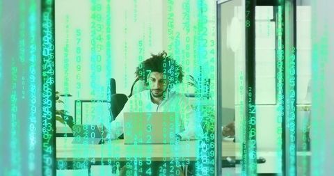 Developer working on laptop behind glass partition with green code overlay in office
