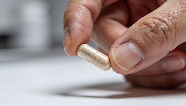 Right Hand Holding Clear Capsule Filled with Powdered Supplement Macro Close-Up
