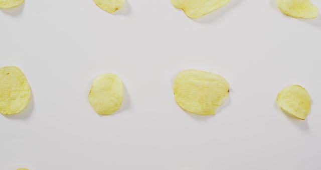 Scattered potato chips on a clean, white background. Great for illustrating snack time indulgence, food patterns, or discussions around unhealthy eating habits. Perfect for marketing materials or blog posts related to food industry, snacks, and recipes.