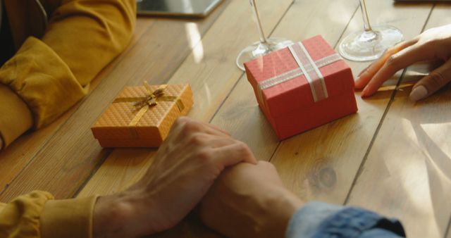 Two people sitting at wooden table, exchanging gifts. Hands touching gently, suggesting a warm, friendly atmosphere