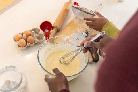 African american friends mixing batter on kitchen countertop, baking together