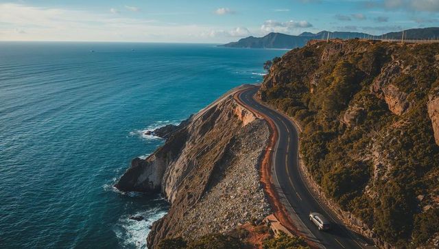 Winding coastal cliff highway hugging ocean with lone car driving at sunset