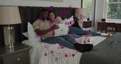 Couple relaxing on bed with laptop and floating iot icons representing connected romance
