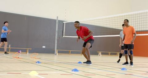 Diverse male teammates practicing volleyball drills on indoor gym court with cones, teamwork