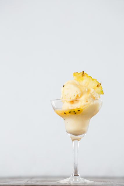 Pineapple ice cream served in an elegant glass, garnished with a pineapple wedge. Perfect for use in food blogs, summer-themed promotions, dessert menus, and tropical-themed events.