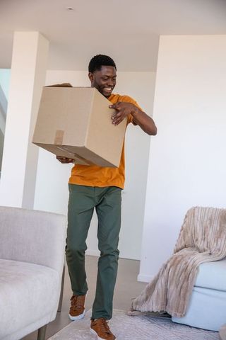 Man smiling holding box in modern living room during move-in