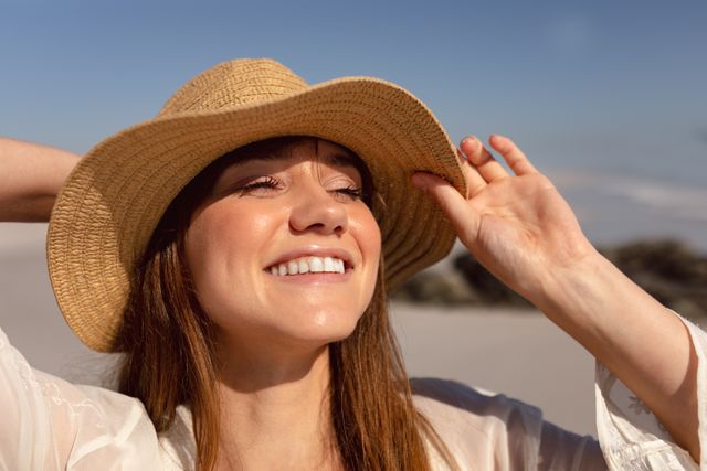 Beautiful young woman in hat looking away on beach in the sunshine