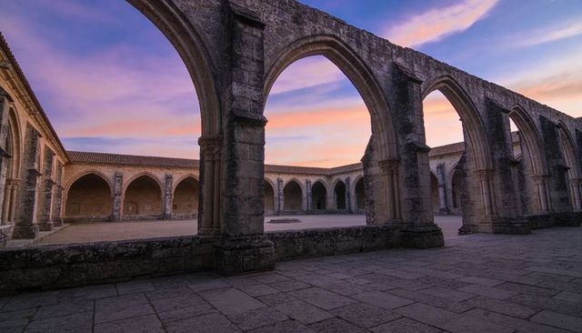 Sunset-lit medieval cloister showcasing weathered stone arches, arcade and quiet courtyard