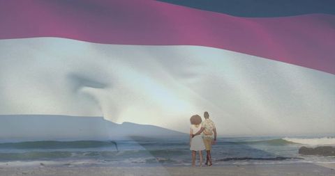 Couple standing on sandy shore facing ocean with translucent pink and white flag overlay