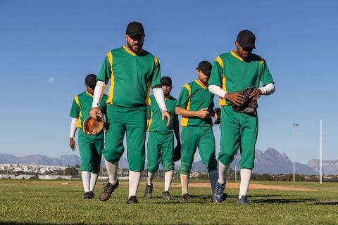 Baseball team walking toward camera in green uniforms holding gloves showing unity
