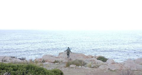 Woman Hiking on Rocky Coastline Overlooking Vast Ocean