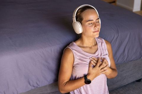 Young woman practicing mindfulness with headphones and smartwatch beside bed