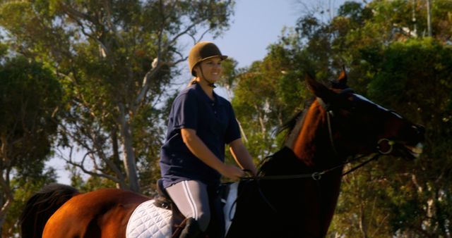 A young Caucasian woman enjoys horseback riding in a sunny outdoor setting, with copy space. Her attire suggests she is an equestrian, engaged in a leisurely ride or training session.