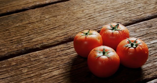 Four fresh tomatoes sitting on a rustic wooden surface with natural light highlighting them, making it perfect for kitchen-themed content, organic food advertising, cookbooks, farm produce presentations, and health-conscious publications.
