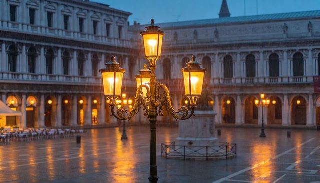 Venice piazza san marco ornate lamppost glowing in rainy evening, wet piazza reflections