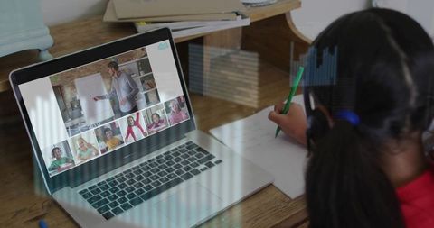Young girl writing at desk during online class on laptop completing worksheet
